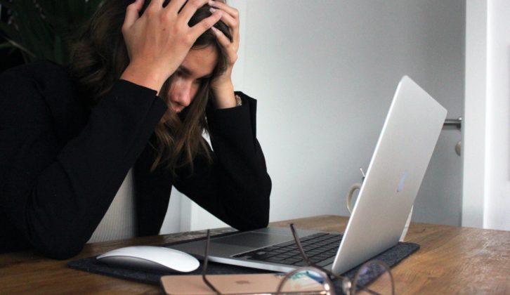 امرأة تمسك برأسها وهي تنظر إلى شاشة الكمبيوتر المحمول.
